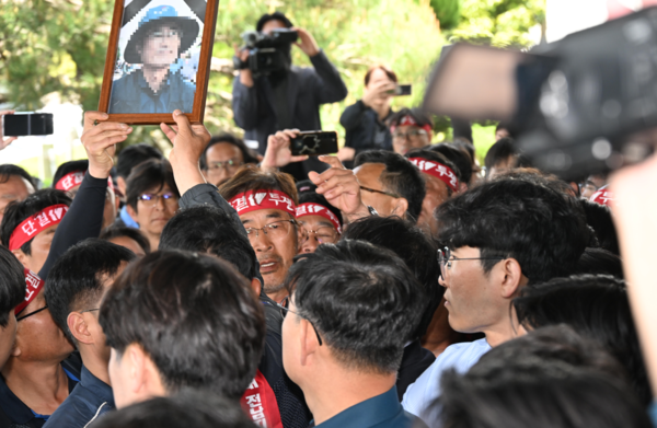21일 화물연대 소속 노동자 등이 희생자 영정사진을 들고 경남경찰청 앞에서 진주 예하리 노동자 사망 관련 CU BGF로지스와 경찰을 규탄하는 화물연대 기자회견을 마친후 항의방문하고 있다. 희생 노동자는 20일 오전 10시 32분께 진주시 정촌면 예하리 BGF로지스 진주센터 인근 민주노총 화물연대 경남지역본부 소속 CU편의점 화물운송 노동자 집회 현장에서 사망했다./김구연 기자