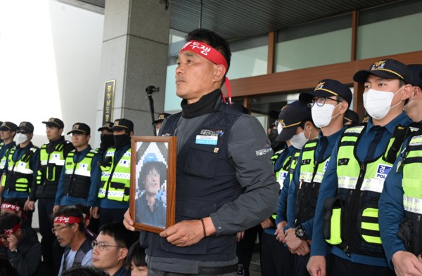 21일 화물연대 소속 노동자 등이 희생자 영정사진을 들고 경남경찰청 앞에서 진주 예하리 노동자 사망 관련 CU BGF로지스와 경찰을 규탄하는 화물연대 기자회견을 마친 후 항의방문하고 있다. 희생 노동자는 20일 오전 10시 32분께 진주시 정촌면 예하리 BGF로지스 진주센터 인근 민주노총 화물연대 경남지역본부 소속 CU편의점 화물운송 노동자 집회 현장에서 사망했다./김구연 기자