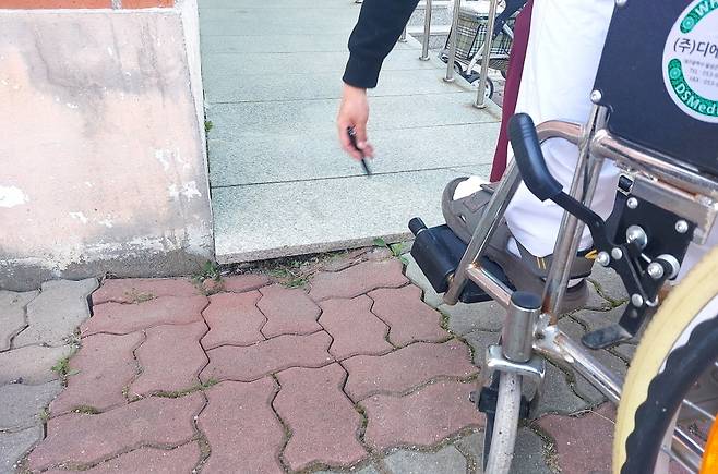 ▲ 포천시 관내의 한 투표소 입구 경사로와 보도블록 사이가 벌어져 있어 휠체어 진입이 불가능한 상태다. 포천나눔의집장애인자립생활센터 관계자가 펜을 이용해 이동약자의 통행을 가로막는 물리적 단차를 지목하고 있다. /사진제공=포천나눔IL센터
