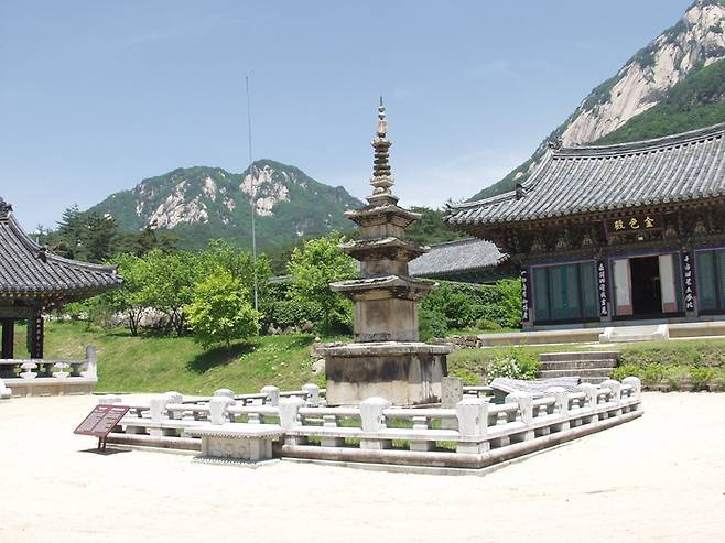 문경 봉암사 경내에 자리한 삼층석탑 전경. 낮은 석재 난간으로 둘러싸인 탑이 중앙에 서 있고, 뒤로는 단청이 화려한 전각과 기와지붕 건물이 이어진다.<강남진기자>