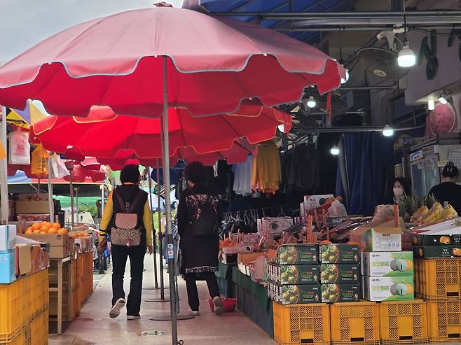 23일 창원 상남 시장에서 시민들이 과일 가게 앞을 지나가고 있다. 창원=이건율 기자