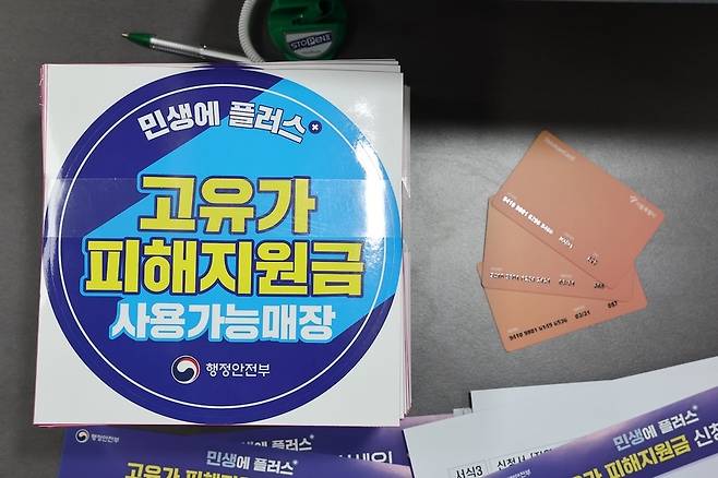 [24일 서울 숭인2동주민센터에 마련된 고유가 피해지원금 신청 창구에 관련 부착물과 사용 카드가 놓여 있다. (사진=연합뉴스)]