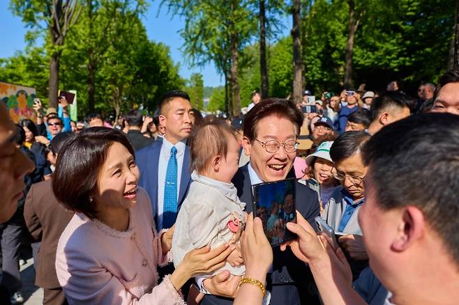 이재명 대통령과 김혜경 여사가 어린이날인 5일 서울 광진구에 있는 서울 어린이대공원을 방문해 아기를 안고 환하게 웃으며 기념사진을 찍고 있다. 이 대통령 부부는 청와대서 첫 어린이날 행사를 마치고 이곳을 깜짝 방문해 시민들의 환호를 받았다. 이 대통령 엑스(X) 계정 캡처