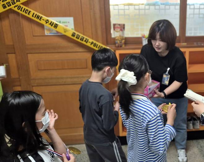 ▲&nbsp;수원동신초등학교 글향기어머니회 회원들이 수사 요원으로 변신해 학생들의 방탈출 미션을 돕고 있다. /사진제공=수원동신초등학교