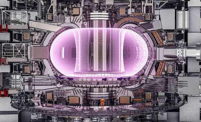 국제핵융합실험로(ITER) 토카막의 내부 구조를 보여주는 개념 단면도. 중앙의 밝게 빛나는 영역이 초고온 플라즈마이며, 강력한 초전도 자석이 이를 공중에 띄운 채 가둔다. 아래쪽에 서 있는 사람과 비교하면 장치 규모를 직관적으로 확인할 수 있다. 국제핵융합실험로기구(ITER Organization) 제공