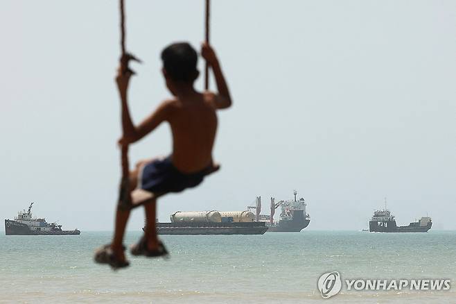 이란 반다르아바스 해변에서 바라본 호르무즈 해협 지난 21일(현지시간) 이란 남부 항구도시 반다르아바스 해변에서 한 아이가 호르무즈 해협에 떠 있는 선박들을 배경으로 그네를 타고 있다. [WANA·로이터=연합뉴스. 재판매 및 DB 금지]