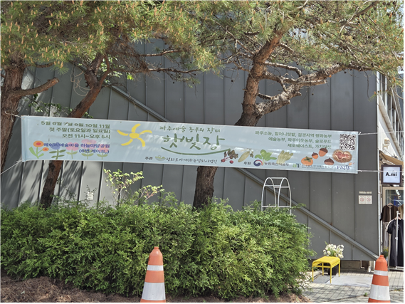 헤이리 예술마을 하늘마당공원에 파주예술 농부의 장터 '햇빛장'을 알리는 현수막이 걸려 있다. 지역 농산물, 예술, 생활장터가 결합된 사례로 마을 자원의 활용 가능성을 보여주고 있다.