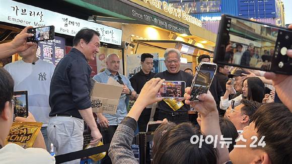 최태원 SK그룹 회장(왼쪽)과 젠슨 황 엔비디아 최고경영자(CEO)가 5일 서울 마포구 홍대 삼겹살집 '형님저요' 앞에서 SK하이닉스 HBM(고대역폭메모리) 과자칩을 들고 시민들과 소통하고 있다. [사진=정유림 기자]