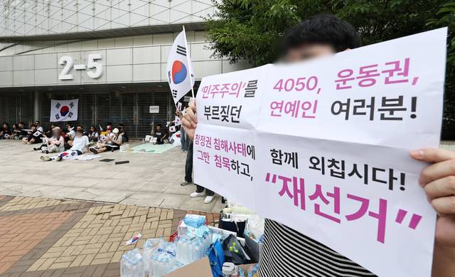 6·3 지방선거 투표지 부족 사태를 규탄하며 재선거를 요구하는 ‘잠실 개표소 봉쇄 시위’가 계속되고 있는 7일 서울 송파구 올림픽공원 핸드볼경기장 앞에서 부정선거를 주장하는 한 시민이 손팻말을 들고 있다. [연합뉴스]