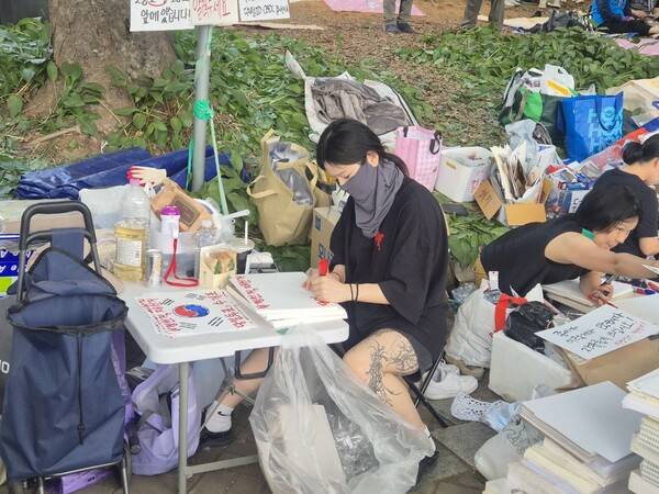 ▲대자보 곁에선 참가자들이 간이책상에 자리를 잡고 앉아 쌓인 종이에 직접 '부정선거 재선거' '전자투표 반대, 수개표' 구호와 태극 문양을 반복해 적고 있었다.사진=김예리 기자