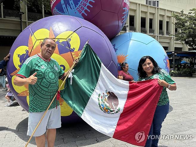 멕시코 국기 들고 기념 사진 찍는 헤수스와 로타 벨라스케스 부부(좌측부터)  (사포판[멕시코 할리스코주]=연합뉴스) 오명언 기자 = 2026북중미 월드컵이 열리는 멕시코 과달라하라 인근 사포판 역사 지구에 있는 보행자 전용 거리에 월드컵 상징 조형물이 설치되어 있다. 7일(현지시간) 축구유니폼을 입은 시민 등이 기념사진을 촬영하고 있다. 2026.6.8 coup@yna.co.kr