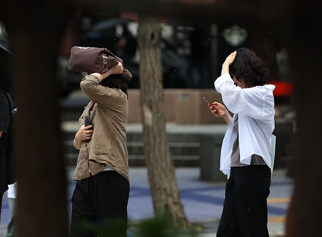 ▲서울 세종로사거리 인근 버스정류장에서 우산을 준비하지 못한 시민들이 손과 가방으로 머리를 가린 채 버스를 기다리고 있다. 사진= 연합뉴스