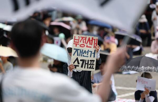 ▲6·3 지방선거 투표용지 부족 사태를 규탄하며 재선거를 요구하는 '잠실 개표소 봉쇄 시위'가 계속되고 있는 6월9일 서울 송파구 올림픽공원 핸드볼경기장에서 한 참가자가 부정선거를 주장하며 수개표를 촉구하는 손팻말을 들고 있다. ⓒ연합뉴스