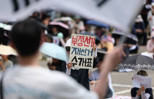 6·3 지방선거 투표용지 부족 사태를 규탄하며 재선거를 요구하는 ‘잠실 개표소 봉쇄 시위’가 계속되고 있는 9일 서울 송파구 올림픽공원 핸드볼경기장에서 한 참가자가 수개표를 촉구하는 손팻말을 들고 있다. 연합뉴스