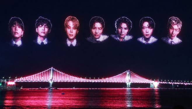 지난 13일 밤 부산 광안리해수욕장에서 열린 BTS 부산공연 기념 특별 드론쇼에서 BTS 멤버 7명의 얼굴이 밤하늘을 수놓고 있다. 사진은 광안대교 경관조명에 이날 선보인 멤버 7명의 얼굴을 합성해 만들었다. 연합뉴스