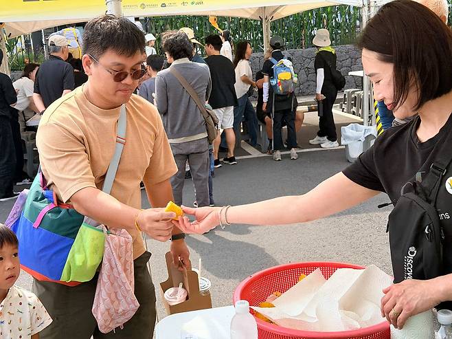 제주를 찾은 싱가폴, 관광객이 2026 수산리 사탕옥수수(초당옥수수) 대잔치 부스에서 시식용 옥수수를 받고 있다. 최충일 기자