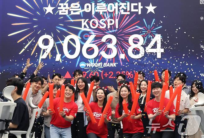 코스피 지수가 전인미답의 9000선 고지를 돌파한 18일 오후 서울 중구 우리은행 본점 딜링룸에서 직원들이 코스피 종가를 배경으로 축하 세리머니를 하고 있다. 코스피는 이날 전일 대비 199.60포인트(2.25%) 오른 9063.84에 장을 마쳤다. 한국 증시는 반도체 대형주의 폭발적인 상승세에 힘입어 지난 5월 26일 장중 8000선을 돌파한 후 불과 16거래일 만에 천의 자리를 바꾸며 '9천피' 시대에 진입했다. ⓒ 뉴스1 오대일 기자