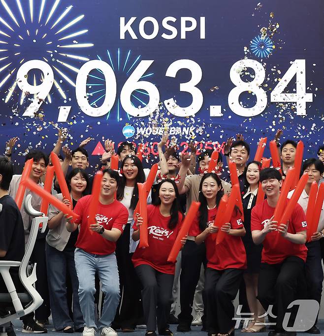 코스피 지수가 전인미답의 9000선 고지를 돌파한 18일 오후 서울 중구 우리은행 본점 딜링룸에서 직원들이 코스피 종가를 배경으로 축하 세리머니를 하고 있다. 2026.6.18 ⓒ 뉴스1 오대일 기자