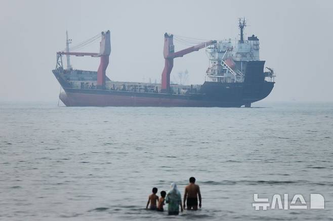 [반다르아바스=AP/뉴시스] 지난 6월30일(현지시간) 이란 반다르아바스 앞 호르무즈 해협에서 화물선 한 척이 정박해 있는 가운데 사람들이 얕은 물에 서 있다. 2026.07.09.