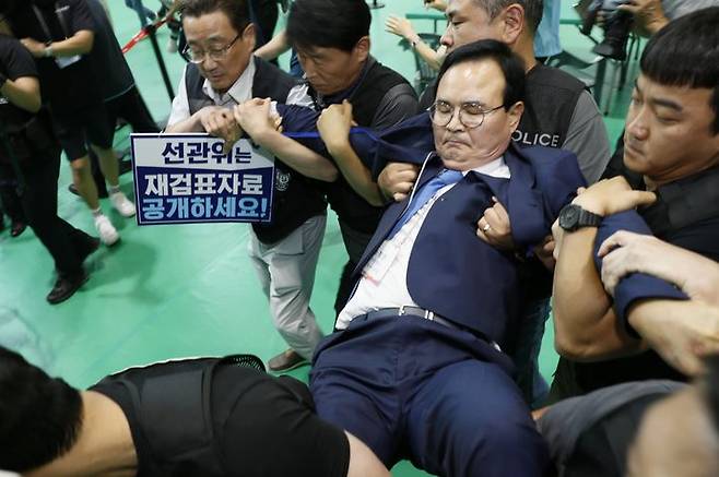 [충주=뉴시스] 이병찬 기자 = 15일 충북 충주 교통대 체육관 충주시장 재검표 개표장에서 민주당 맹정섭 전 충주시장 후보가 강제 퇴거 당하고 있다.2026.07.15.bclee@newsis.com