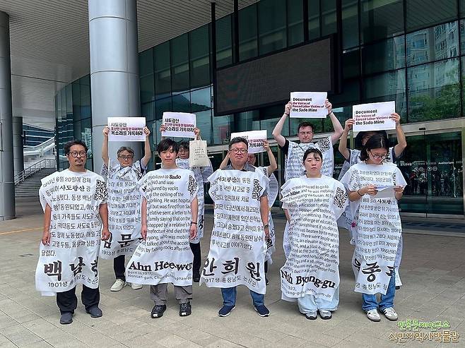 '사도광산 진실 외면 말라' (부산=연합뉴스) 민족문제연구소와 연구소 부설 식민지역사박물관, 일제강제동원시민모임 등 시민단체 회원들이 21일 유네스코 세계유산위원회가 열리고 있는 부산 벡스코 회의장 인근에서 강제 동원 조선인 탄광 노동자들의 이름이 적힌 대자보를 입고 퍼포먼스를 하고 있다. 2026.7.21 [민족문화연구소 제공. 재판매 및 DB 금지] photo@yna.co.kr