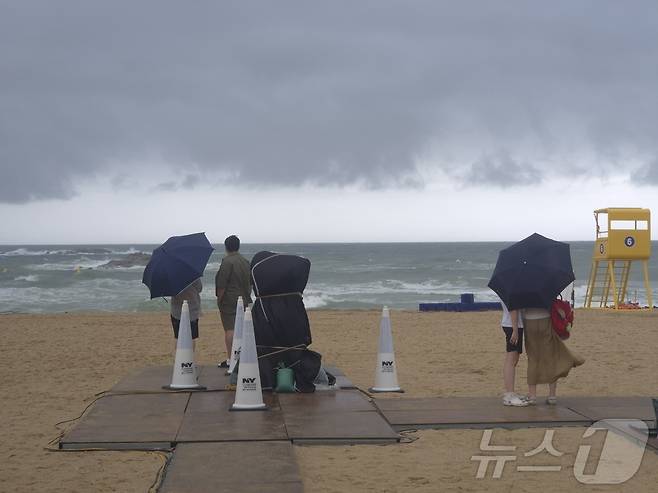 8일 강릉시 경포해수욕장을 찾은 피서객들이 우산을 쓴 채 거센 파도가 이는 바다를 바라보고 있다.   2026.8.8 ⓒ 뉴스1 윤왕근 기자