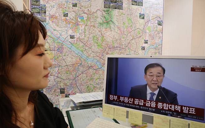 13일 서울 한 부동산 중개업소에서 관계자가 정부의 ‘전월세 및 매매시장 안정을 위한 주택 신속공급 방안’과 ‘부동산 시장 안정을 위한 금융 종합대책’을 TV로 보고 있다. [연합]