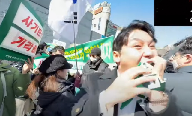 ▲고(故)배인규 신남성연대 대표가 2025년 이화여대 정문 앞에서 탄핵 찬성 측 피켓을 뺏어 찢은 뒤 씹어 먹고 있다.ⓒ신남성연대 유튜브 갈무리