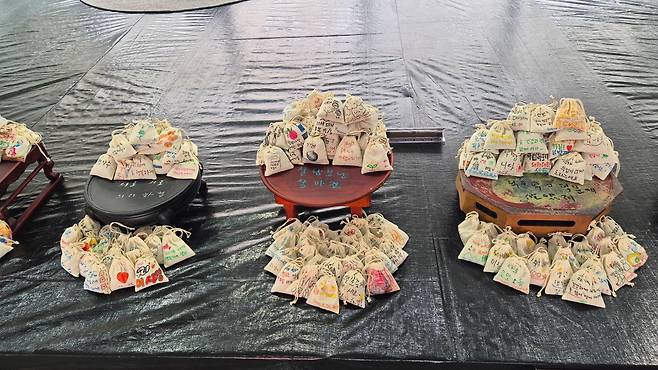 제주비엔날레가 열리는 제주도립미술관 로비에 설치된 연미의 '비가 오면 비를 맞고, 바람이 불면 바람을 맞고, 햇살이 비추면 햇살을 받고'는 제주의 강인한 생명력을 뜻하는 토종 푸른콩을 주머니에 넣고 그 위에 도민들의 소원을 적어 쌓아올린 작품이다. 함께 놓인 밥상은 제주 할머니들이 오랜 세월 실제 사용한 밥상으로, "어떤 힘으로 살아왔는가"란 질문에 대한 답을 직접 적었다. 제주=인현우 기자