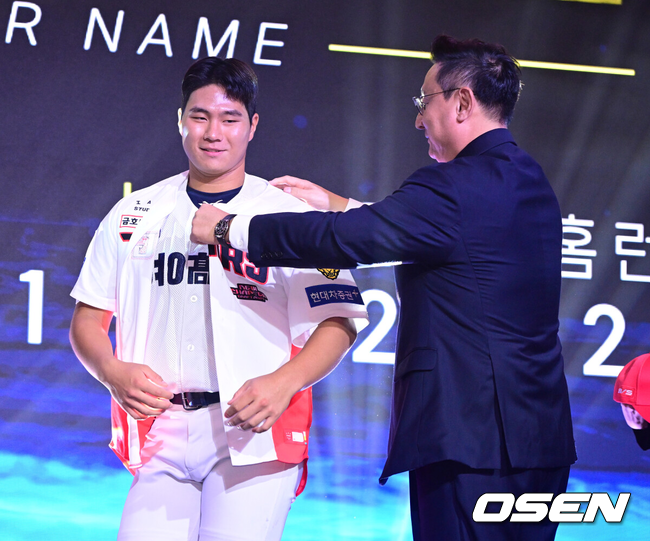 [OSEN=최규한 기자] 21일 오후 서울 잠실동 롯데호텔 월드 크리스탈볼룸에서 ‘2027 KBO 신인드래프트’가 열렸다. 이번 신인드래프트는 2025시즌 순위의 역순에 따라 키움 히어로즈, 두산 베어스, KIA 타이거즈, 롯데 자이언츠, KT 위즈, NC 다이노스, 삼성 라이온즈, SSG 랜더스, 한화 이글스, LG 트윈스 순서로 1라운드부터 11라운드까지 지명할 수 있다. 경남고 이호민이 전체 3번으로 KIA 타이거즈에 지명된 뒤 심재학 단장에게 유니폼을 전달받고 있다. 2026.09.21 / dreamer@osen.co.kr