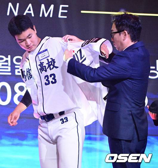 [OSEN=최규한 기자] 21일 오후 서울 잠실동 롯데호텔 월드 크리스탈볼룸에서 ‘2027 KBO 신인드래프트’가 열렸다. 이번 신인드래프트는 2025시즌 순위의 역순에 따라 키움 히어로즈, 두산 베어스, KIA 타이거즈, 롯데 자이언츠, KT 위즈, NC 다이노스, 삼성 라이온즈, SSG 랜더스, 한화 이글스, LG 트윈스 순서로 1라운드부터 11라운드까지 지명할 수 있다. 유신고 이승원이 KT 1라운드에 지명된 뒤 나도현 단장에게 유니폼을 전달받고 있다. 2026.09.21 / dreamer@osen.co.kr