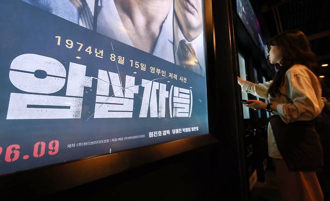 역사 왜곡 비판을 받고 있는 영화 '암살자(들)'의 홍보 포스터를 한 관객이 살펴보고 있다./뉴스1