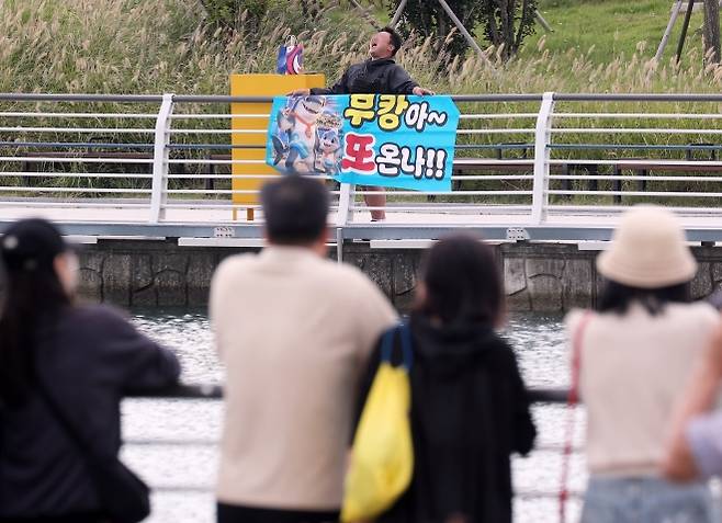 “부캉아~ 또 온나” - 지난달 29일 부산 동구 북항 친수공원 수로에서 관계자들이 선박과 워터펌프를 동원해 상어 ‘부캉이’를 외해로 유도하기 전 한 시민이 부캉이를 응원하는 현수막을 들고 소리 지르고 있다. 뉴스1