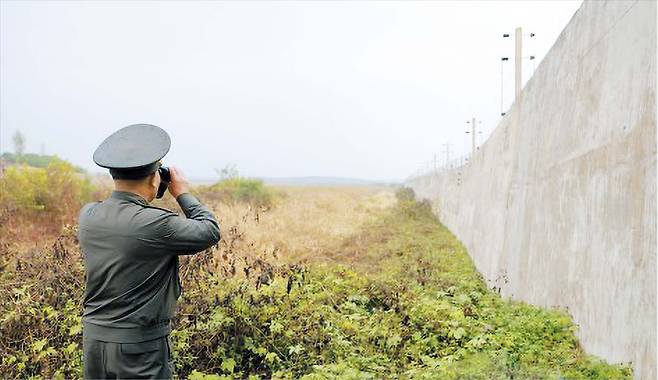 박정천(뒷모습) 북한 국방성 고문이 21일 군사분계선(MDL) 인근 지역에서 망원경으로 남측을 바라보고 있다. 오른쪽으로 북한군이 2024년 4월 이후 새로 건설한 콘크리트 대전차 방벽이 보인다. 북한은 이날 김여정 노동당 부장과 박정천 등이 ‘남부 국경 요새화’ 공사 현장을 시찰했다고 보도했다. /조선중앙통신 연합뉴스
