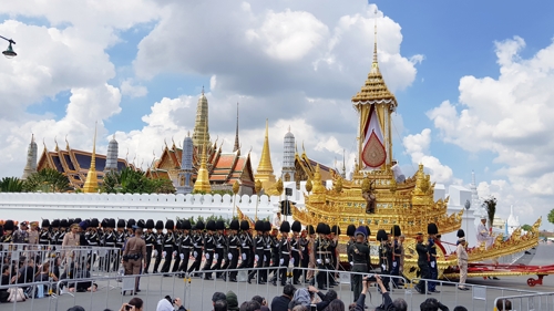 푸미폰 국왕의 시신을 왕궁에서 장례식장인 사남루엉 광장으로 운구하는 왕실 전차가 왕궁 앞을 지나는 가운데 시민들이 이 장면을 지켜보고 있다.