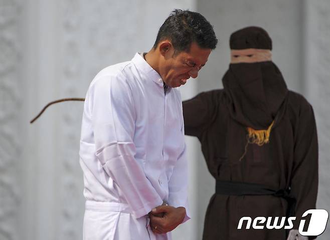 인도네시아 기독교인 조노 심볼론이 지난달 19일 아체주 반다 아체에 있는 이슬람 사원 앞에서 시민들이 보는 가운데 태형을 받고 있다. 그는 주류 판매로 샤리아법(이슬람율법)을 위반했다는 이유로 처벌을 받았다. © AFP=뉴스1