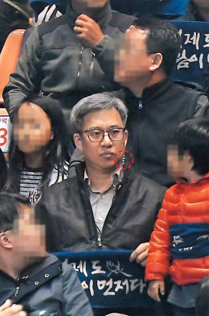 작년 3월 민주당 대선 경선장… ‘이어 마이크’ 낀 드루킹 - ‘민주당원 댓글 조작’ 사건 주범인 김동원(필명 드루킹)씨가 작년 3월 31일 부산 연제구 부산실내체육관에서 열린 더불어민주당 영남권 대선 경선 현장에서 자신이 주도한 조직인 ‘경인선(경제도 사람이 먼저다)’ 회원들과 함께 ‘경제도 사람이 먼저다’라고 적힌 파란색 수건을 들고 있는 모습. 당시 김씨는 관중석에서 왼쪽 귀에 ‘이어 마이크’를 꽂은 채 시종일관 심각한 표정을 지었다. 왼쪽 상의 위로 나온 이어 마이크 줄(빨간 점선 부분)이 김씨 귀 뒷부분으로 연결된 것이 보인다. 통상 이어 마이크는 현장 상황을 통제하는 관계자들이 서로 연락을 주고받기 위해 사용하는 경우가 많다. /뉴데일리 제공