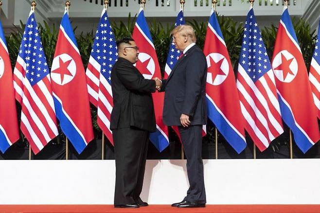 트럼프 미국 대통령과 김정은 북한 국무위원장이 12일(현지시간) 싱가포르 카펠라 호텔에 마련된 회담장에서 만나 악수를 나누고 있다. 뒷편의 성조기와 인공기가 일렬로 배치되어 있다. (사진=백악관 제공)