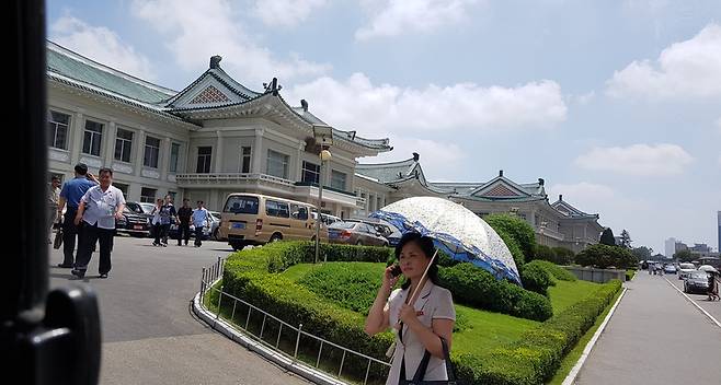 지난 18일 낮 평양의 냉면 전문점인 옥류관 건물 앞에서 평양의 한 여성이 양산으로 해를 가린 채 휴대폰 통화를 하고 있다.  김한정 의원 제공