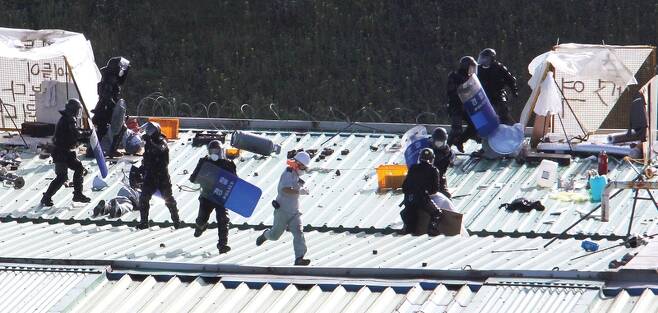 2009년 8월5일 조립공장 옥상에서 고 김주중씨(오른쪽 상단에서 솥뚜껑으로 몸을 가린 사람)가 경찰 특공대의 방패와 전투화에 찍히며 진압 당하고 있다. 금속노조 쌍용자동차지부 제공