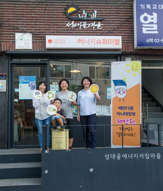 에너지자립마을 ‘성대골’ 주민들이 서울 동작구 상도동에 설립된 에너지슈퍼마 앞에서 에너지전환 로고를 들고 환하게 웃고 있다. 성대골 에너지자립마을 제공