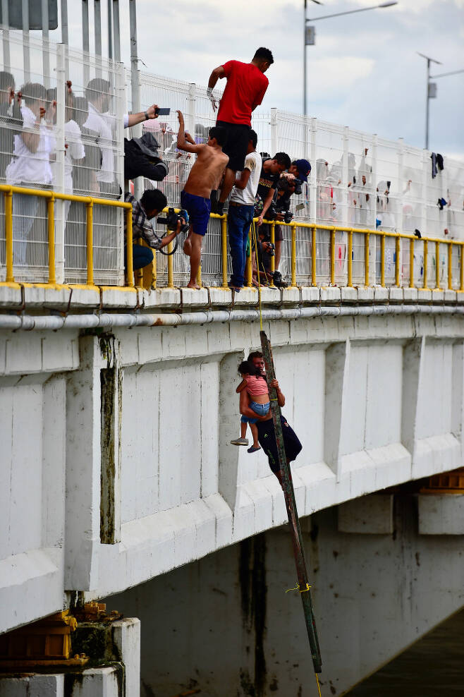 과테말라·멕시코 국경도시 시우다드 이달고에서 20일(현지시간) 온두라스 이민자들이 아이를 안고 강을 건너려는 다른 이민자를 도와주고 있다. AFP=연합뉴스
