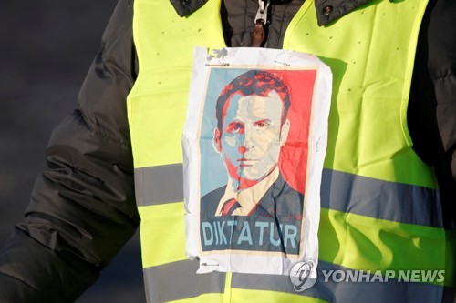 프랑스의 노란 조끼를 입은 시위자가 가슴에 에마뉘엘 마크롱 대통령의 초상과 그 아래 '독재자'라고 적힌 종이를 붙였다.  [로이터=연합뉴스]