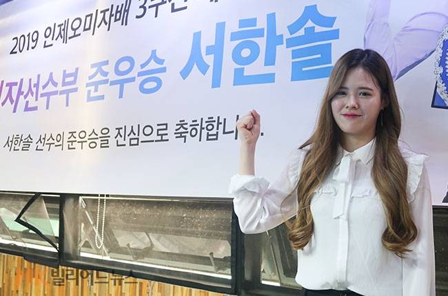 서한솔이 연습구장 한 켠에 걸린 축하 현수막 앞에서 포즈를 취하고 있다.