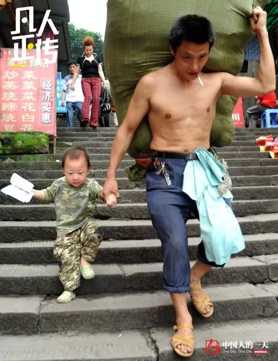 충칭시 차오톈먼 도매시장의 짐꾼 란광후이가 2010년 등엔 짐을, 오른손으론 세 살 아들의 손목을 잡고 계단을 내려오고 있다. [중국 인민망 캡처, 쉬캉핑]