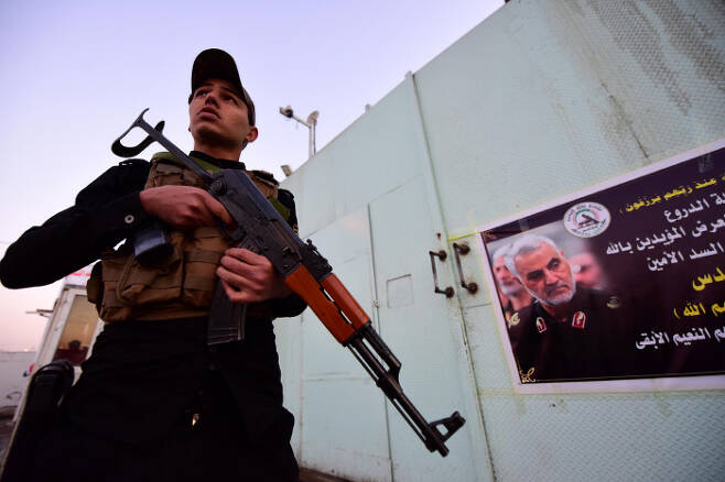 이라크 바그다드에서 7일 친이란 민병대 조직원이 가셈 솔레이마니 전 이란 쿠드스 특수부대 사령관의 사진 옆에 총을 들고 서 있다.  바그다드 | EPA연합뉴스