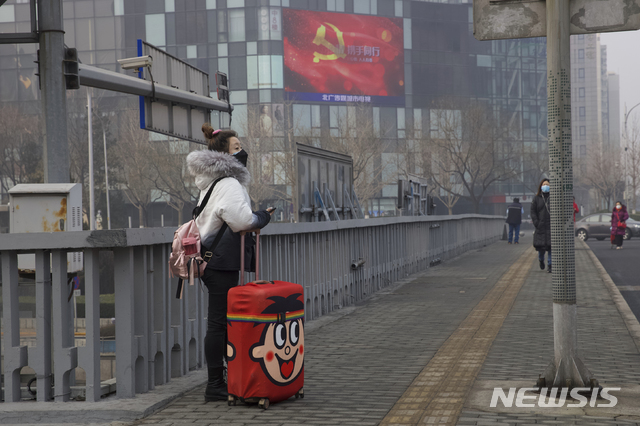 [베이징=AP/뉴시스] 신종 코로나바이러스감염증(코로나19)이 퍼지고 있는 가운데 13일(현지시간) 중국 베이징의 한 다리 위에 여행가방을 끌고 있는 여성이 마스크를 낀 채 서 있는 모습. 뒷편 전광판에 코로나19와 싸우자는 중국 정부의 홍보 문구가 쓰여 있다. 2020.02.14.
