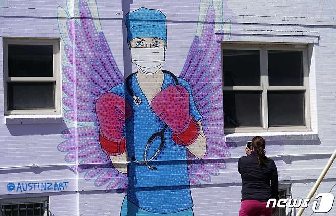 미국 덴버 시내에서 한 여성이 복싱 장갑과 천사 날개, 마스크를 착용한 의료인을 묘사한 벽화 앞에서 스마트폰을 이용해 촬영을 하고 있다.  © AFP=뉴스1 © News1 이동원 기자