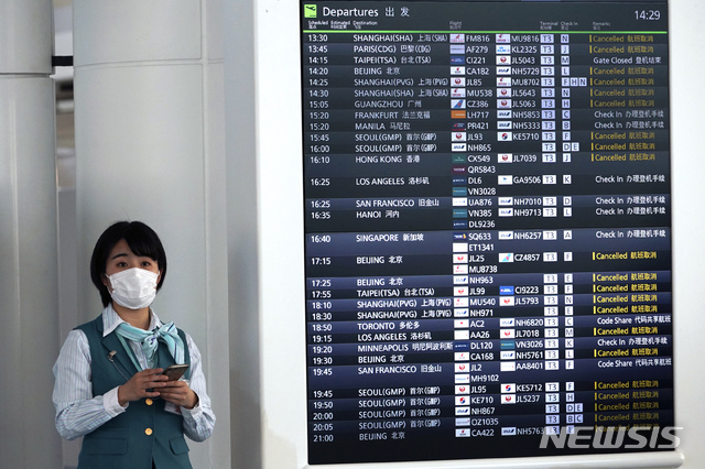[도쿄=AP/뉴시스]지난  3월18일 일본 도쿄 하네다 공항에 마스크를 쓴 직원이 신종 코로나바이러스 감염증(코로나19)로 취소된 항공 스케줄을 표시한 전광판 옆에 서 있다. 2020.03.19.