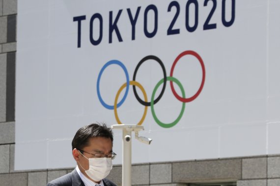 마스크를 쓴 한 남성이 도쿄도청 외벽에 걸린 도쿄올림픽 로고 앞을 지나고 있다. AP뉴시스